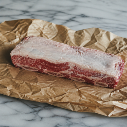 Rauwe short rib met bot en zichtbare vetlaag op bruin papier