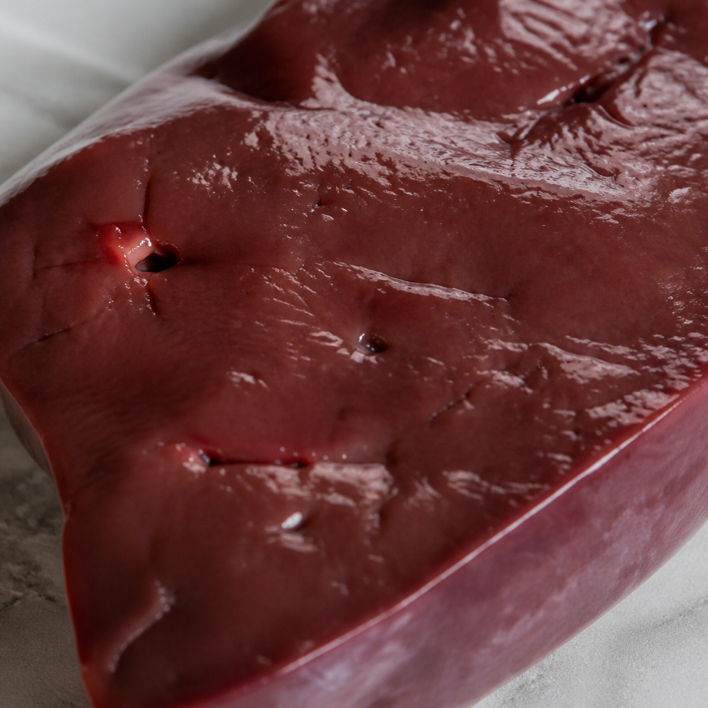 Rauw kalfslever in close-up, met glanzend donkerrood oppervlak en zichtbare snijvlakken