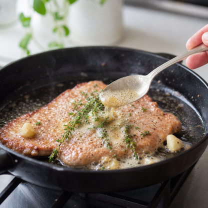Gebakken kalfs schnitzel in koekenpan met boter, knoflook en tijm