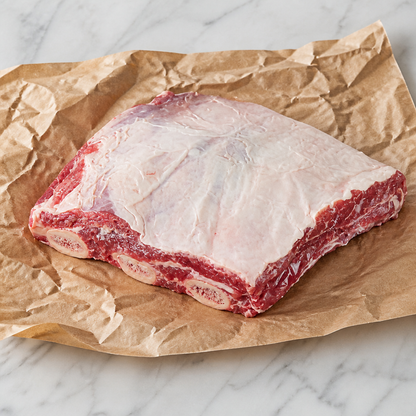 Rauw stuk rundershort rib met bot, op bruin papier op een licht marmeren ondergrond