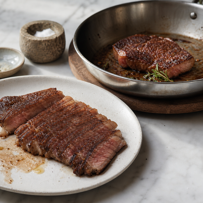 Gesneden Wagyu rib-eye met roze kern op bord, met nog een stuk in koekenpan